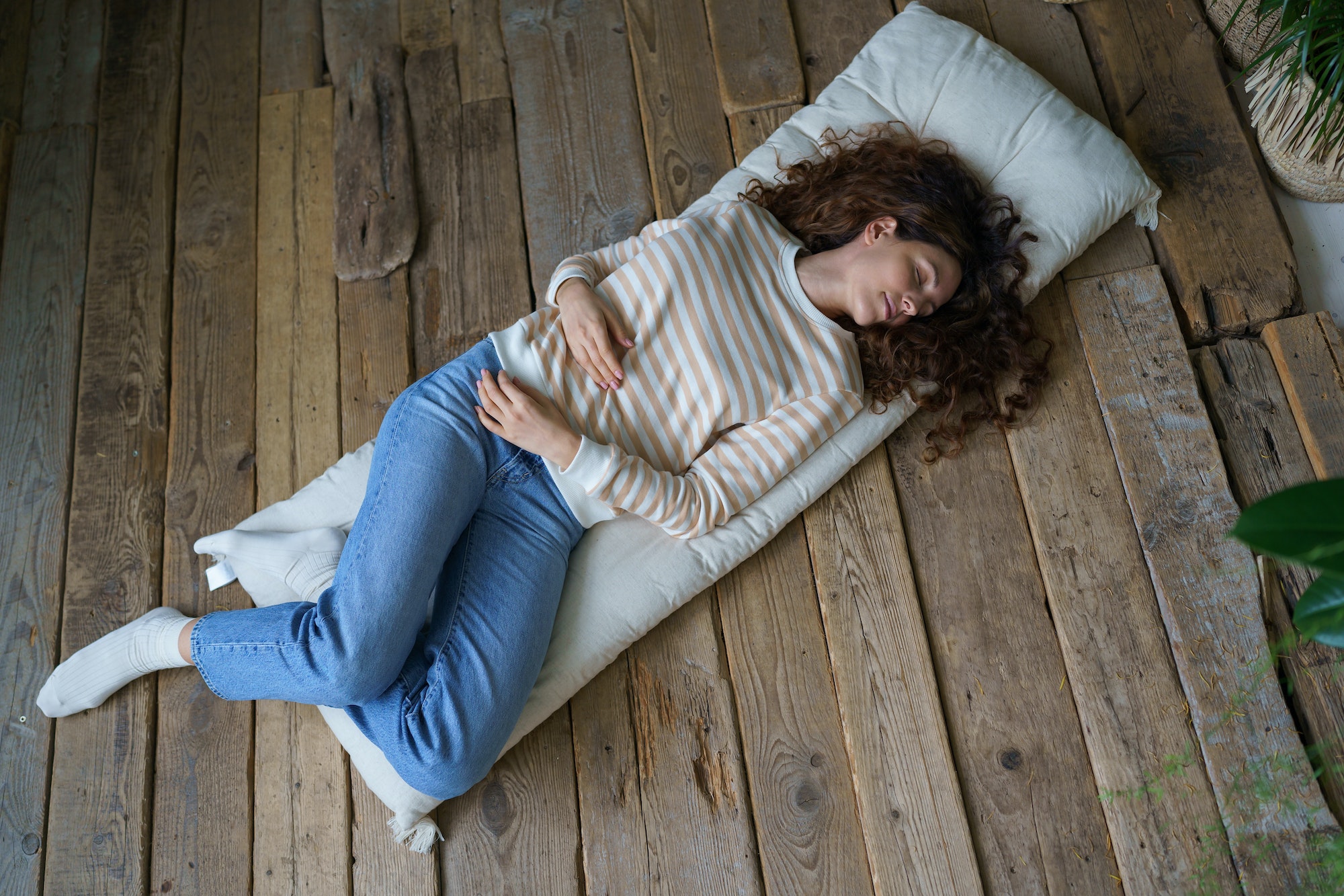 Beautiful young calm woman sleeping, napping during day on mattress on wooden floor at cozy home